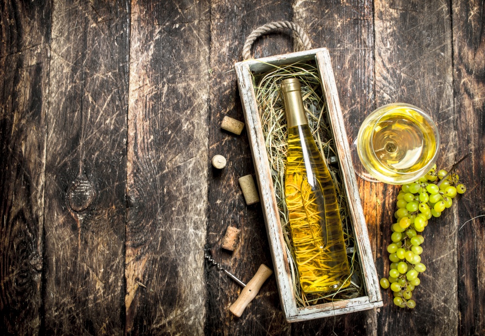 White wine in old box with green grapes. On a wooden background.. White wine in old box with green grapes.