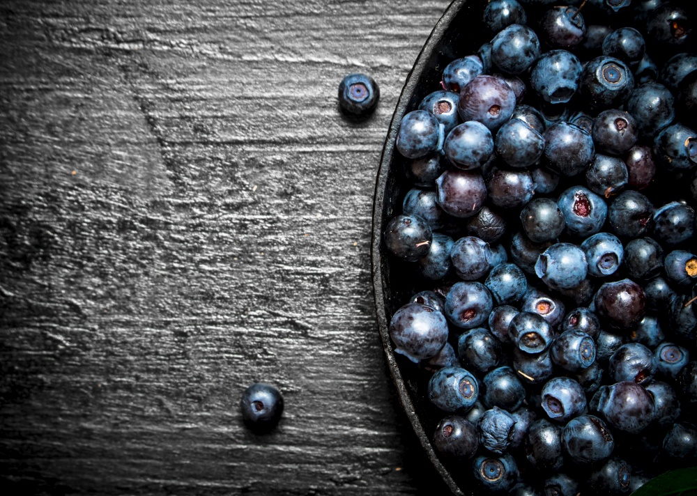 Blueberries in an old plate . On a black wooden background.. Blueberries in an old plate . On black wooden background.