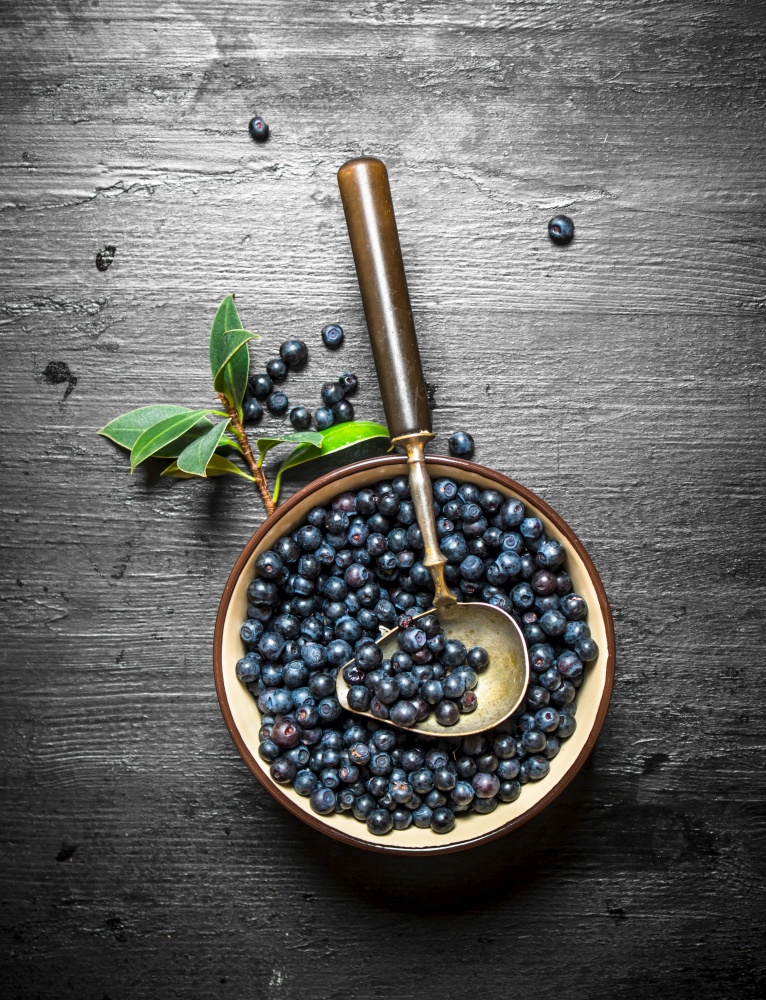 Blueberries in a Cup with a spoon. On a black wooden background.. Blueberries in cup with a spoon.