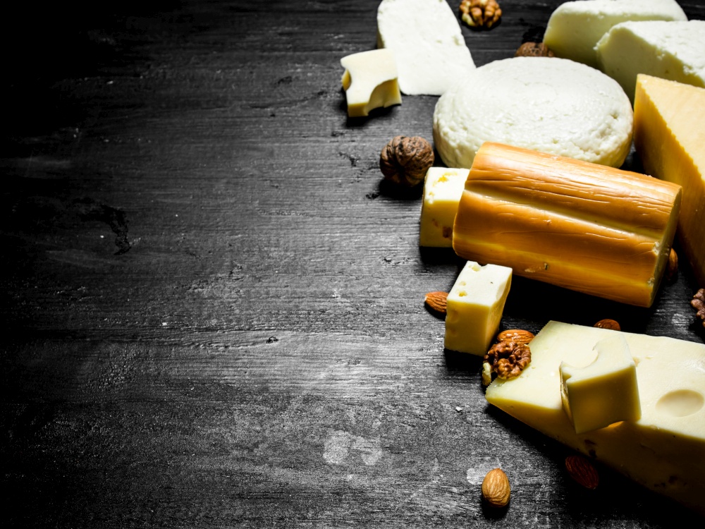Different pieces of cheese with nuts. On a black wooden background.. Different pieces of cheese with nuts.