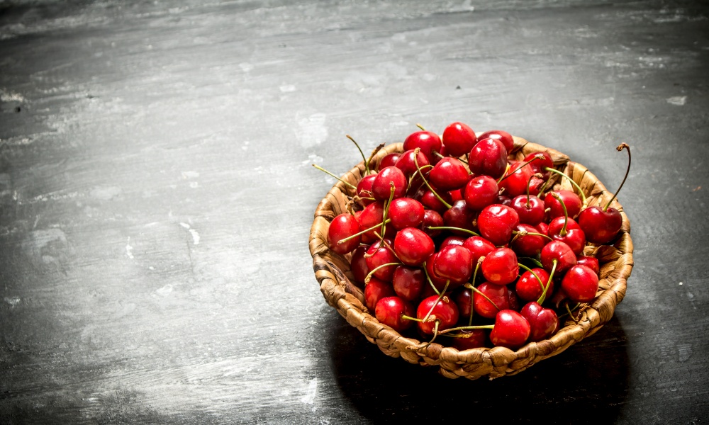 Cherry in the basket. On a black wooden background.. Cherry in the basket.