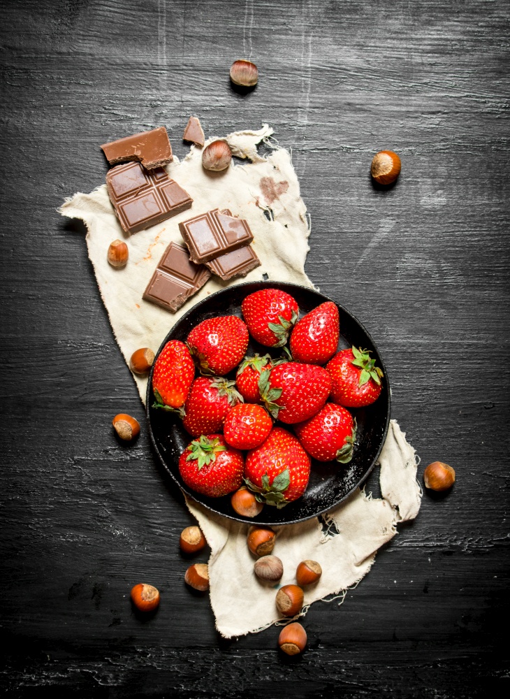 Strawberries with slices of chocolate and nuts. On the black wooden table.. Strawberries with slices of chocolate and nuts.