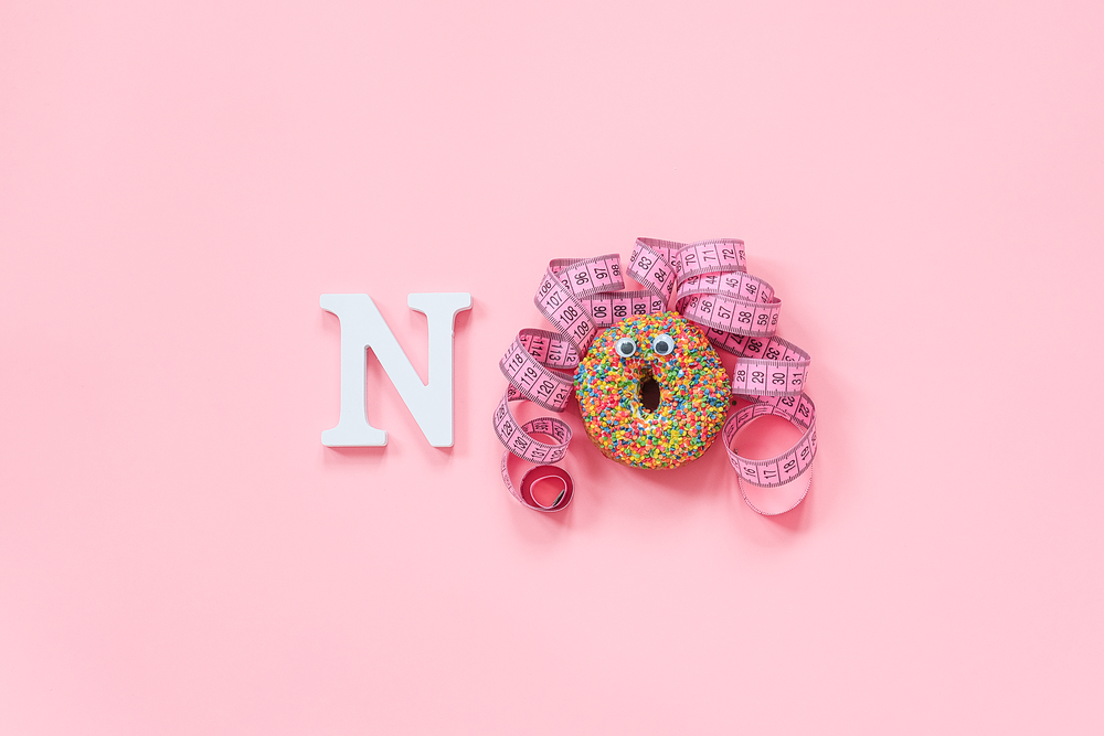 Funny face of woman from donut with eyes and hair from centimeter tape on plate and text no on pink background. Concept diet and abandonment of dounuts, fast food, unhealthy food.. Funny face of woman from donut with eyes and hair from centimeter tape on plate and text no on pink background. Concept diet and abandonment of dounuts, fast food, unhealthy food