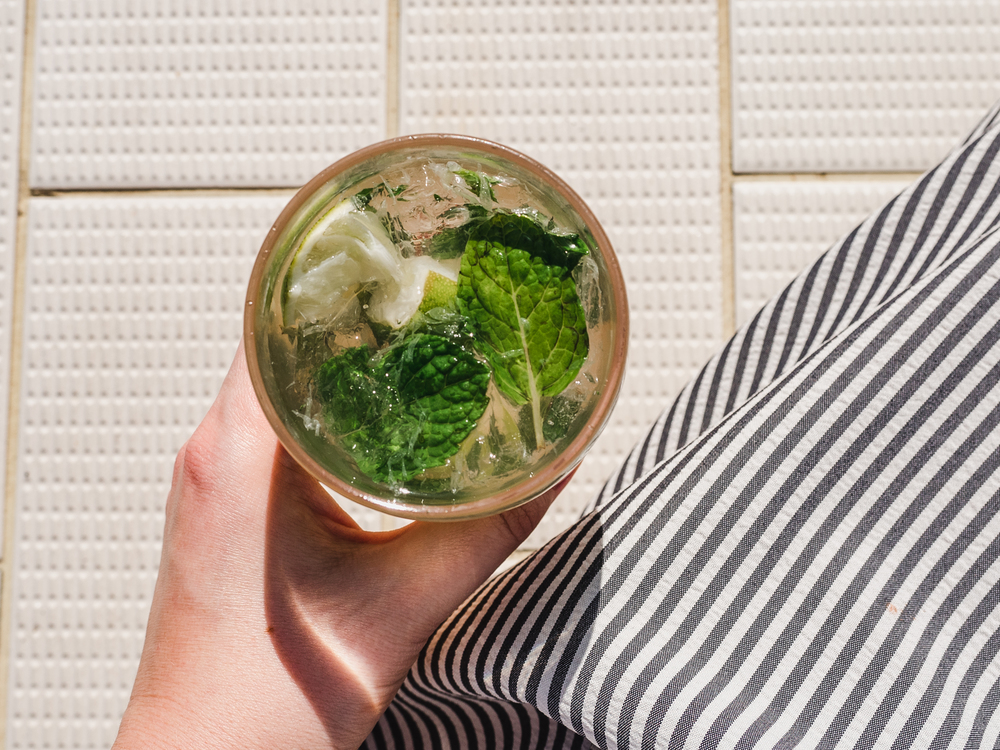 Beautiful glass with refreshing mojito and ice cubes on the background of the plank deck. Top view, close-up. Concept of leisure and travel. Beautiful glass with refreshing mojito and ice cubes