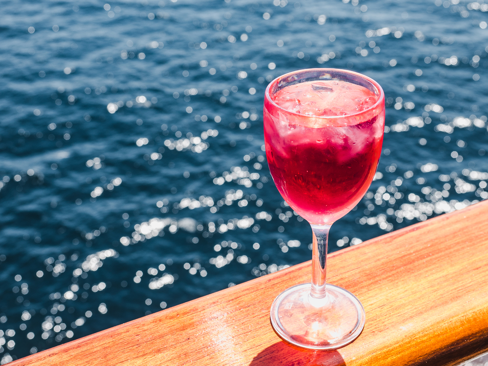 Beautiful glass of pink wine on the open deck of a cruise liner against the backdrop of blue sea waves. Side view, close-up. Concept of leisure and travel. Man holding a beautiful glass of pink wine