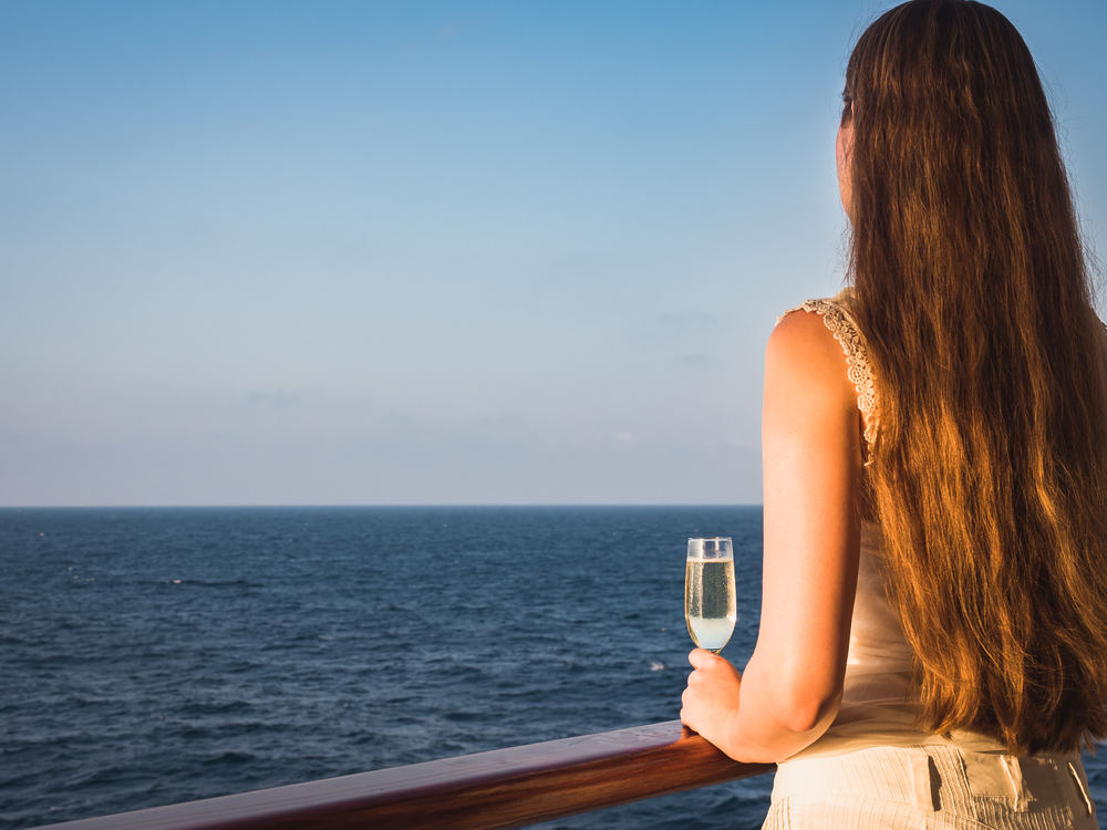 Fashionable woman holding a beautiful glass on the open deck of a cruise liner against the backdrop of blue sea waves. Side view, close-up. Concept of leisure and travel. Woman holding a glass on the deck