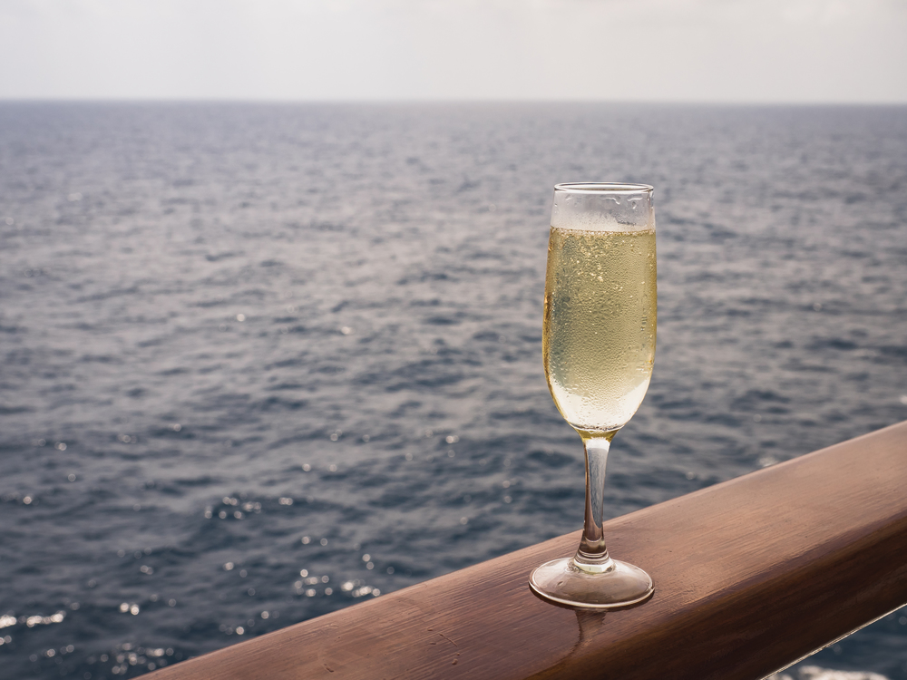 Beautiful champagne glass on the open deck of a cruise liner against the backdrop of blue sea waves. Side view, close-up. Concept of leisure and travel. Beautiful champagne glass on the open deck