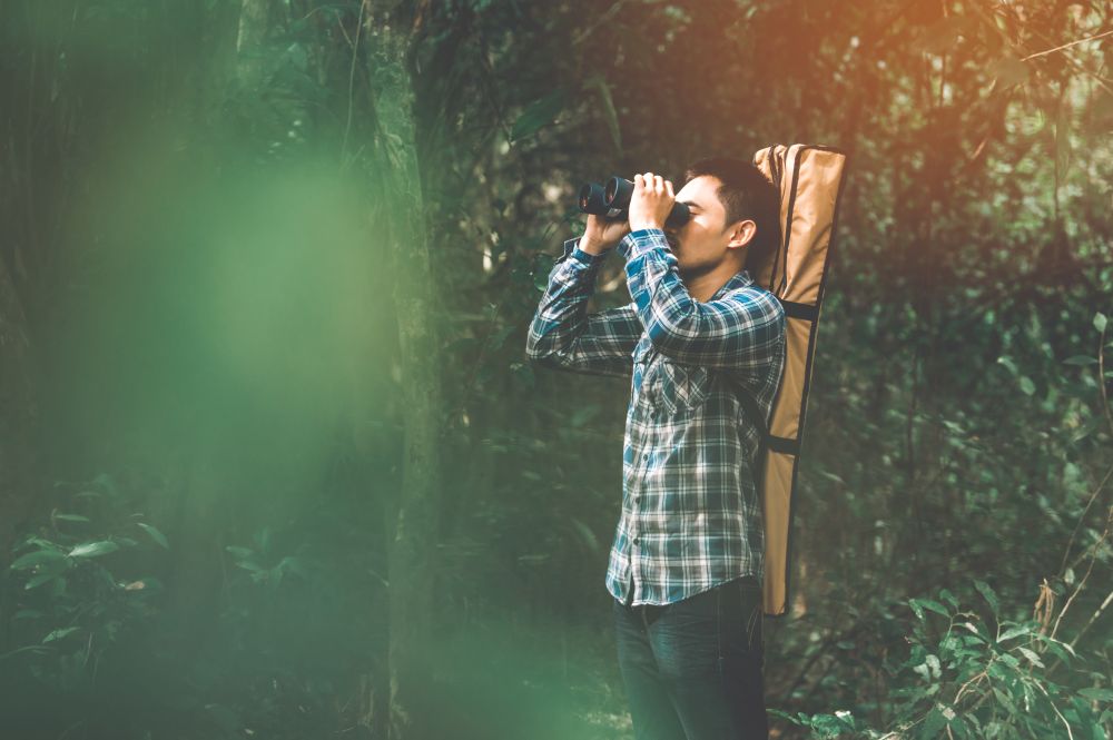 Man with binoculars telescope in forest looking destination as lost people or foreseeable future. People lifestyles and leisure activity concept. Nature and backpacker traveling jungle background