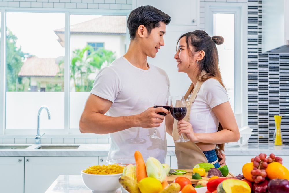 Happy Asian young married couple drinking wine and looking each other in home kitchen. Boyfriend and girlfriend cooking together. People lifestyle and romantic relationship concept. Valentines day