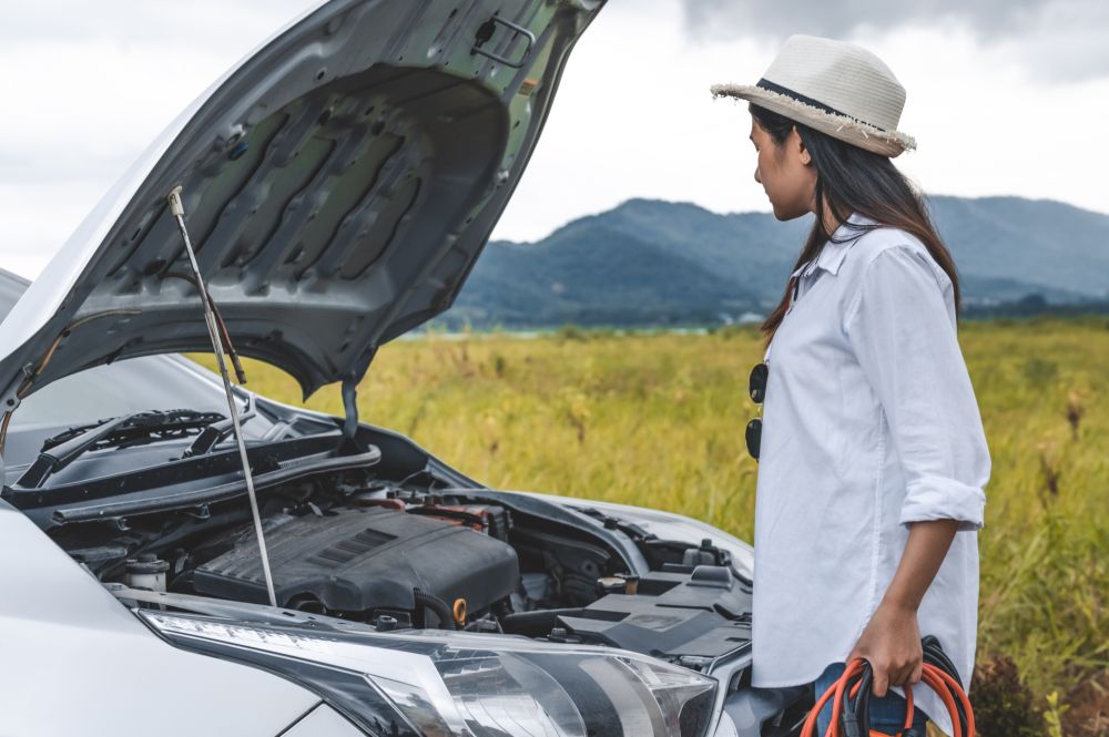 Asian woman holding battery booster cable copper wire for repairing breakdown broken car by connect with red and black line to electric terminal by herself. Car maintenance and transportation concept