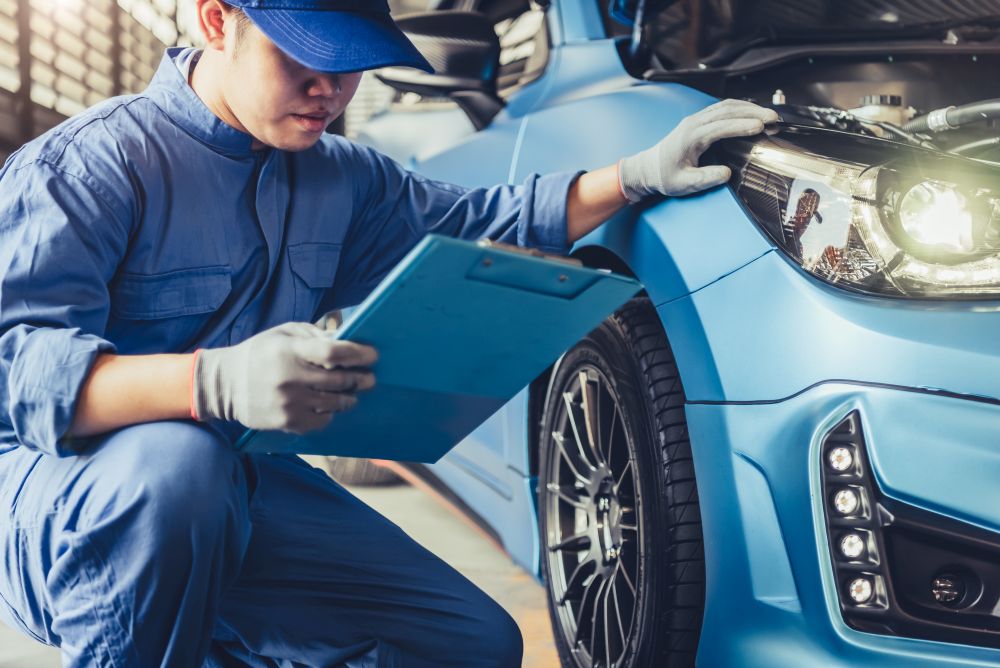 Asian car mechanic technician holding clipboard and checking to maintenance vehicle by customer claim order in auto repair shop garage. Wheel tire repair service. People occupation and business job