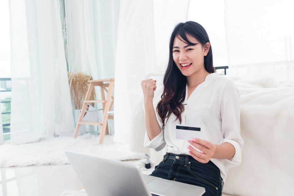 Young Asian woman use credit card for online shopping with laptop. Business and Banking payment concept. Price sale and promotion concept. Technology and Computer theme. E-commerce and Marketing theme