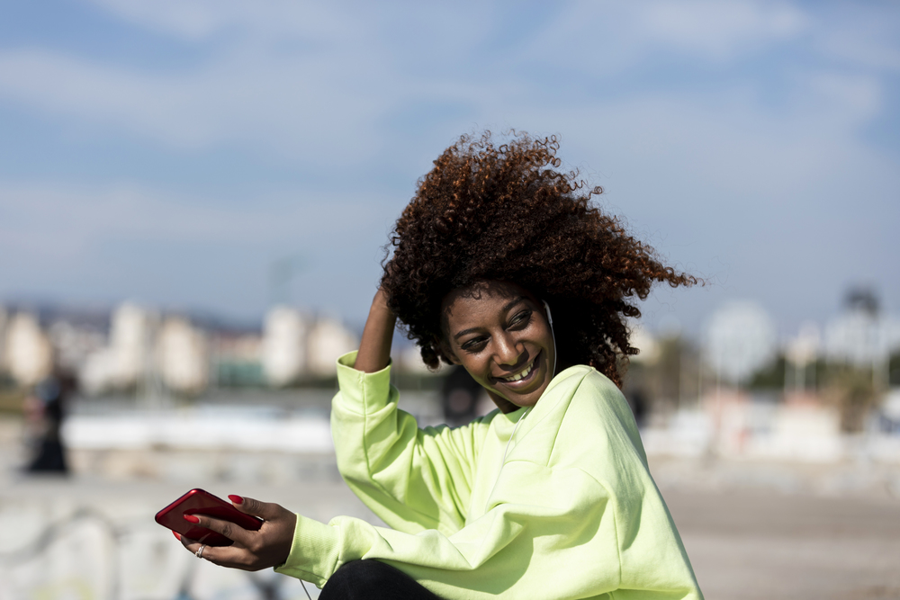 Afro american woman sitting on shore using a mobile phone in a sunny day