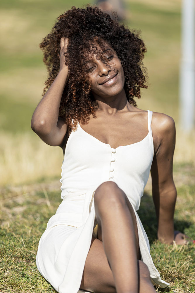 Afro american woman with white dress sitting on grass in a park in sunny day