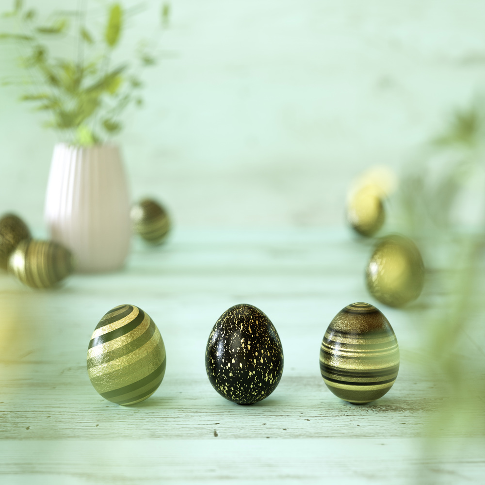 Three gold and black Easter eggs decorated with stripes, splatter, flowers and spots in gold, black and yellow on mint green wood background with copy space for your holiday greeting in square format