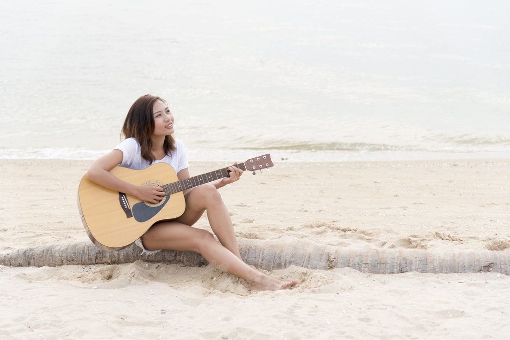 young woman playing guitar on the beach. Musician lifestyle. Travel concept.