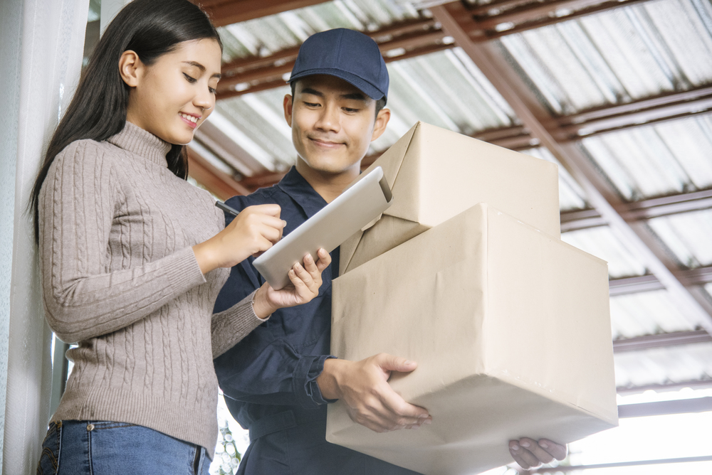 Delivery mail shipping package services . Young deliveryman in uniform shipping goods package to recipient from shopping online and signing for got parcel package service on clipboard.