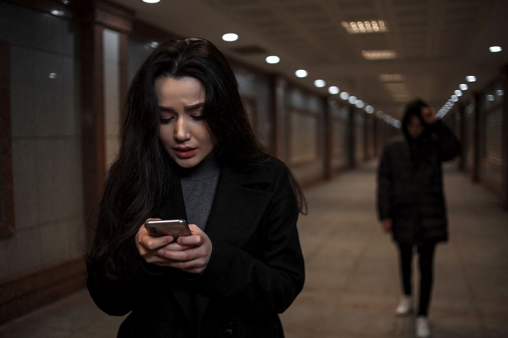 a young beautiful woman walks through an underground passage at night, followed by a man in dark clothing with a hood on his head. a woman tries to dial the number of the rescue service on the phone