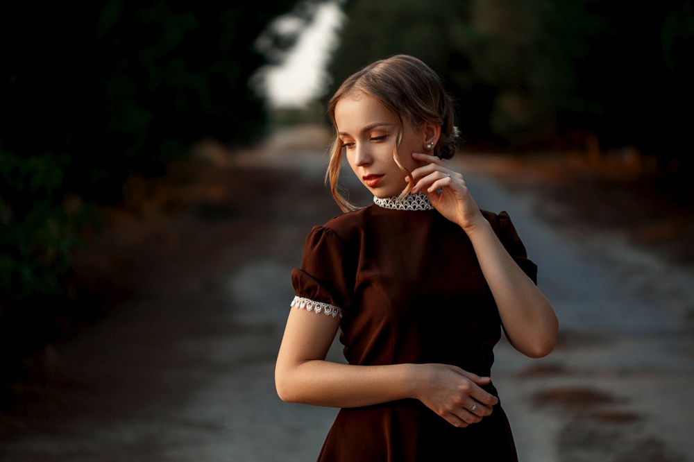 close-up portrait of a young beautiful girl in a brown dress in a retro style on an abandoned road.