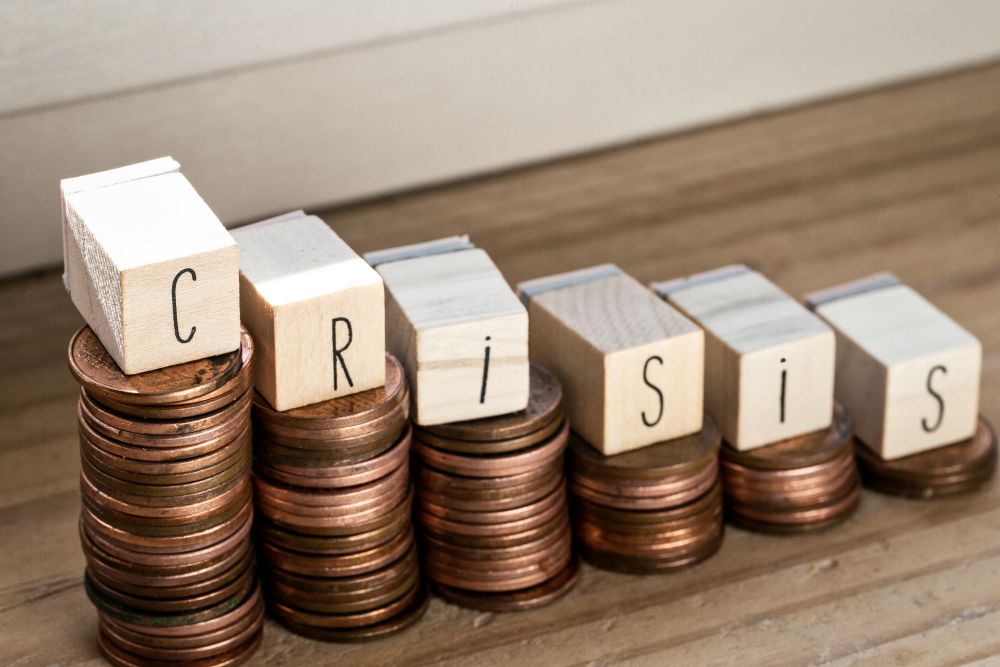 Wooden cubes with the word Crisis and pile of coins, money climbing stairs, business concept background. Wooden cubes with the word Crisis and pile of coins, money climbing stairs, business concept