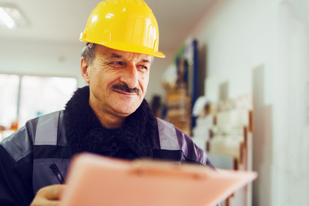 Portrait of caucasian senior man construction worker general laborer building contractor wearing yellow protective helmet holding pen and document checking data report project in the office warehouse