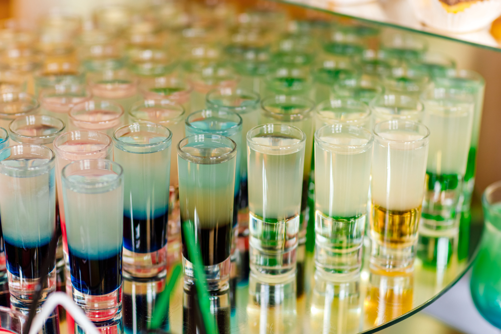 Many different colorful alcoholic shot cocktails in drinking glasses green brown red and white colors standing on mirror table on bar. set of alcohol mini cocktail shooters. Many different colorful alcoholic shot cocktails in drinking glasses green brown red and white colors standing on mirror table on bar. set of alcohol mini cocktail shooters.