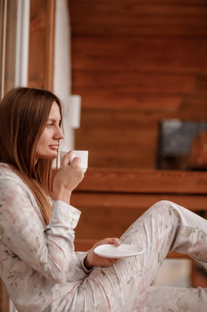 young woman in stylish nightwear enjoy drinking coffee or tea outdoor on balcony in the morning and looks at the mountains.