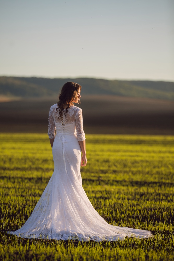 A beautiful bride in a sleek wedding dress stands with her back to a gloomy spring field. A beautiful bride in a sleek wedding dress stands with her back to a gloomy spring field.