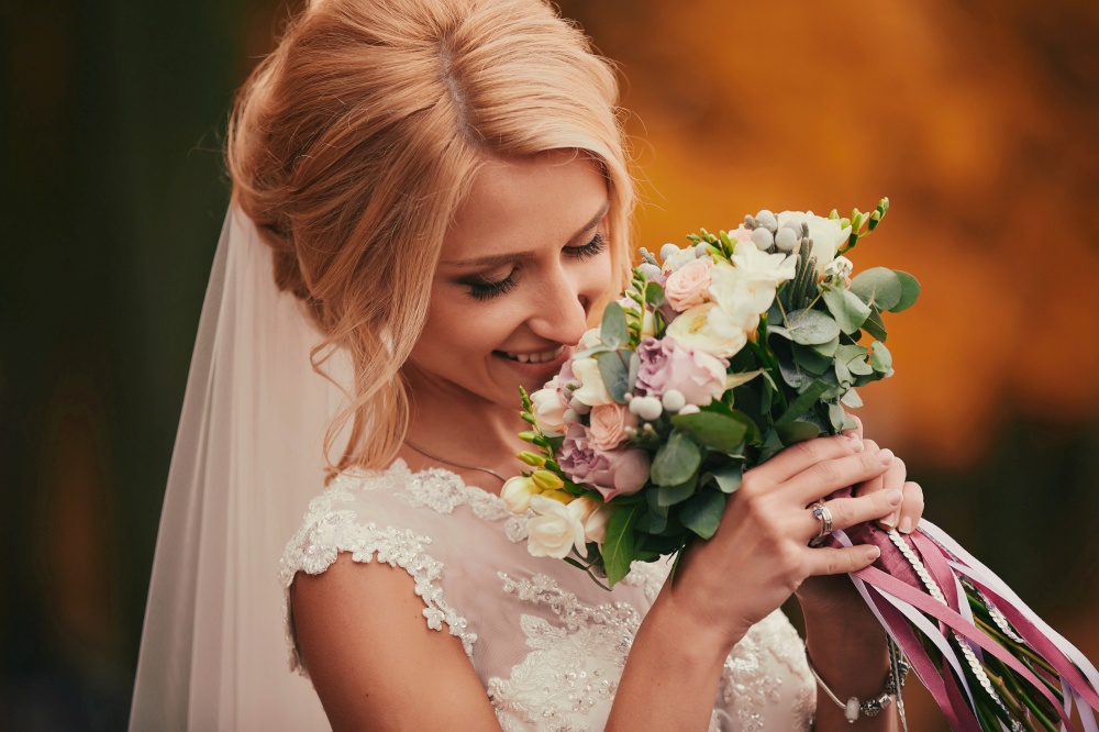 Beautiful bride smelling wedding bouquet in autumn park close up on wedding day.. Beautiful bride smelling wedding bouquet in autumn park close up on wedding day
