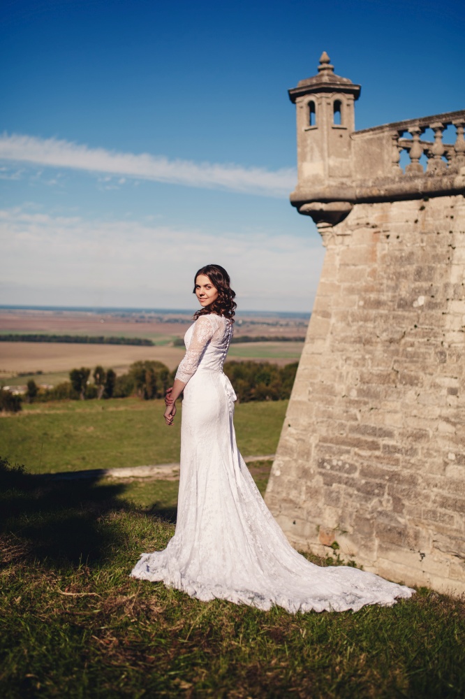 Young bride in a wedding dress posing against the backdrop of an old castle.. Young bride in a wedding dress posing against the backdrop of an old castle