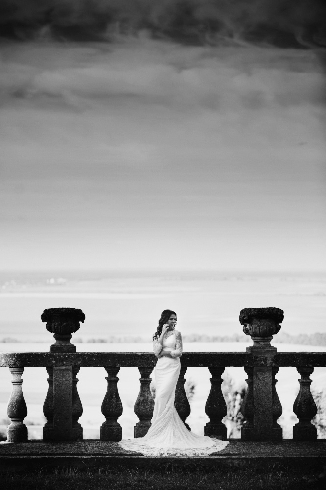 A beautiful bride in a luxurious dress stands on a large balcony. Black and white photo.. A beautiful bride in a luxurious dress stands on a large balcony. Black and white photo