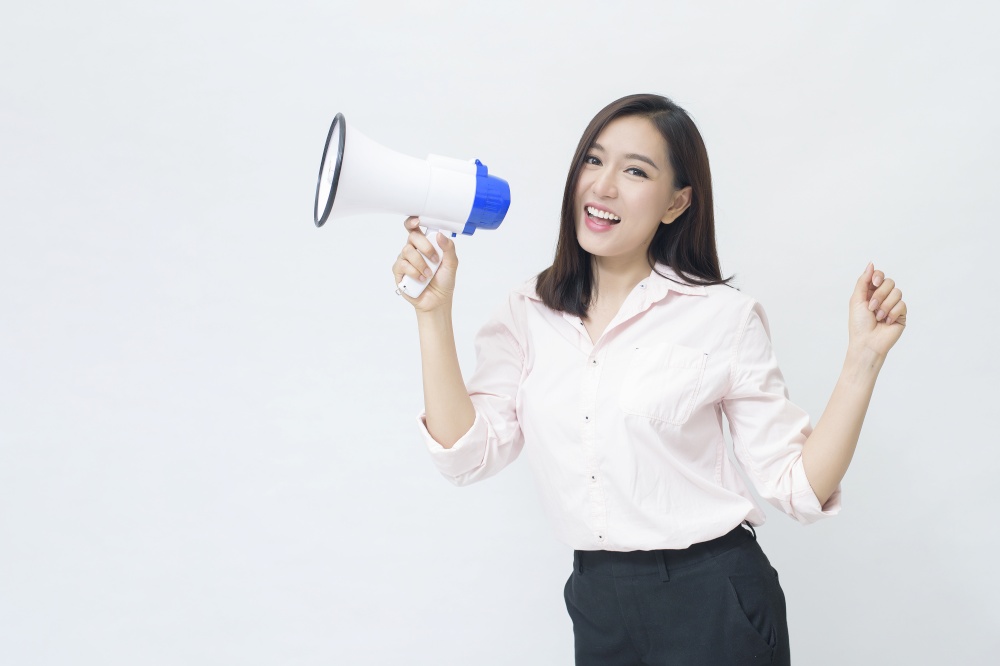 A young beautiful Asian woman is announcing by megaphone on white background .. A young beautiful Asian woman is announcing by megaphone on white background
