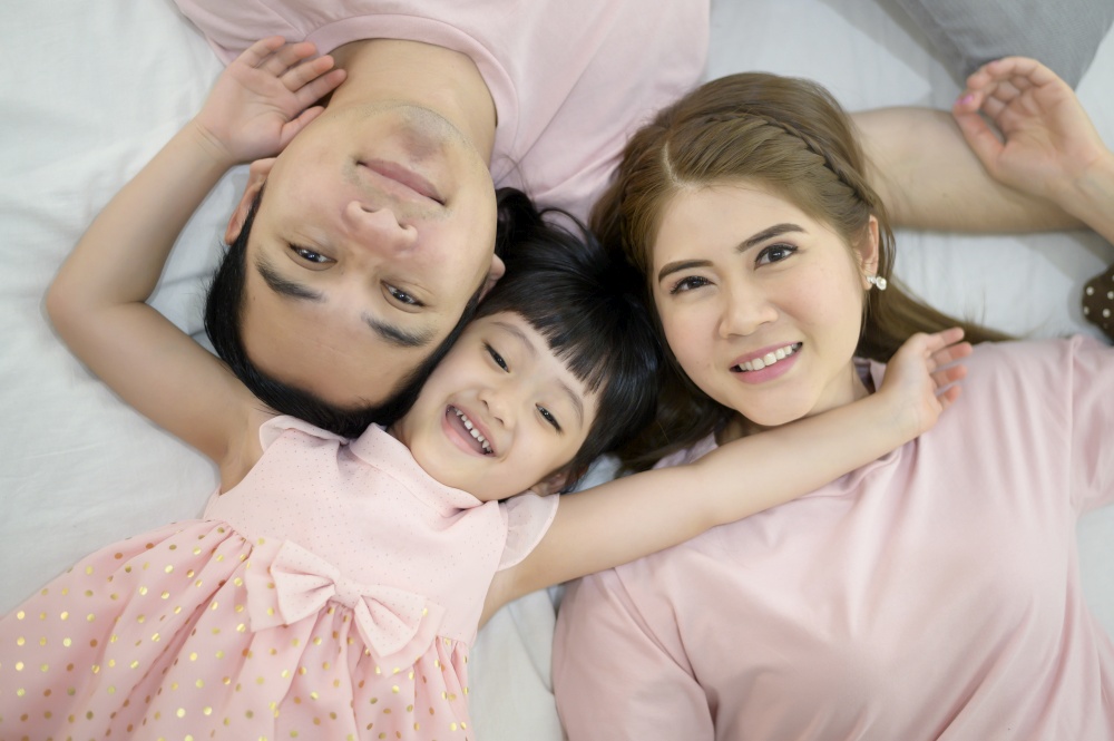 Top view of a happy asian family wearing pink shirt portrait on white bed indoor