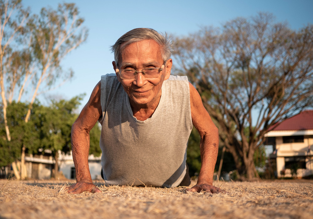 Asian elderly men with gray hair in sportswear doing push ups in the park on summer day. Healthy lifestyle and Healthcare concept.