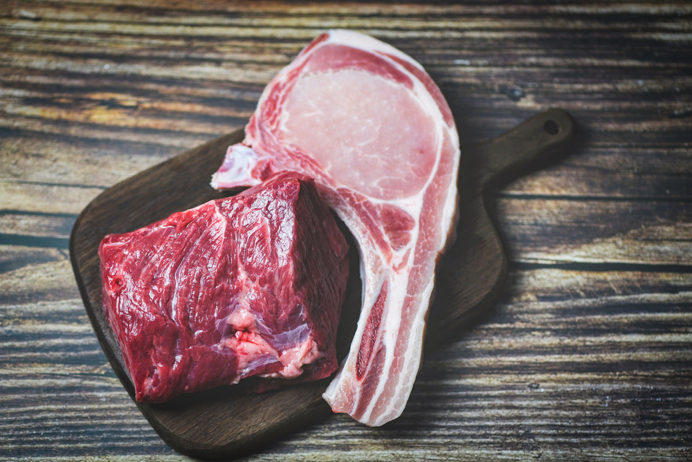 Fresh meat beef sliced and pork chops on wooden cutting board background / Raw beef steak