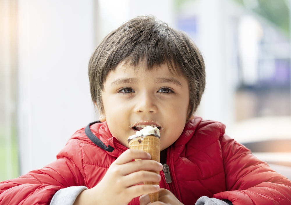 Portrait of happy child eating an ice cream, Smiling kid boy sitting in cafe with a happy face enjoying his an ice cream in spring or summer. Family relaxing on weekend concept