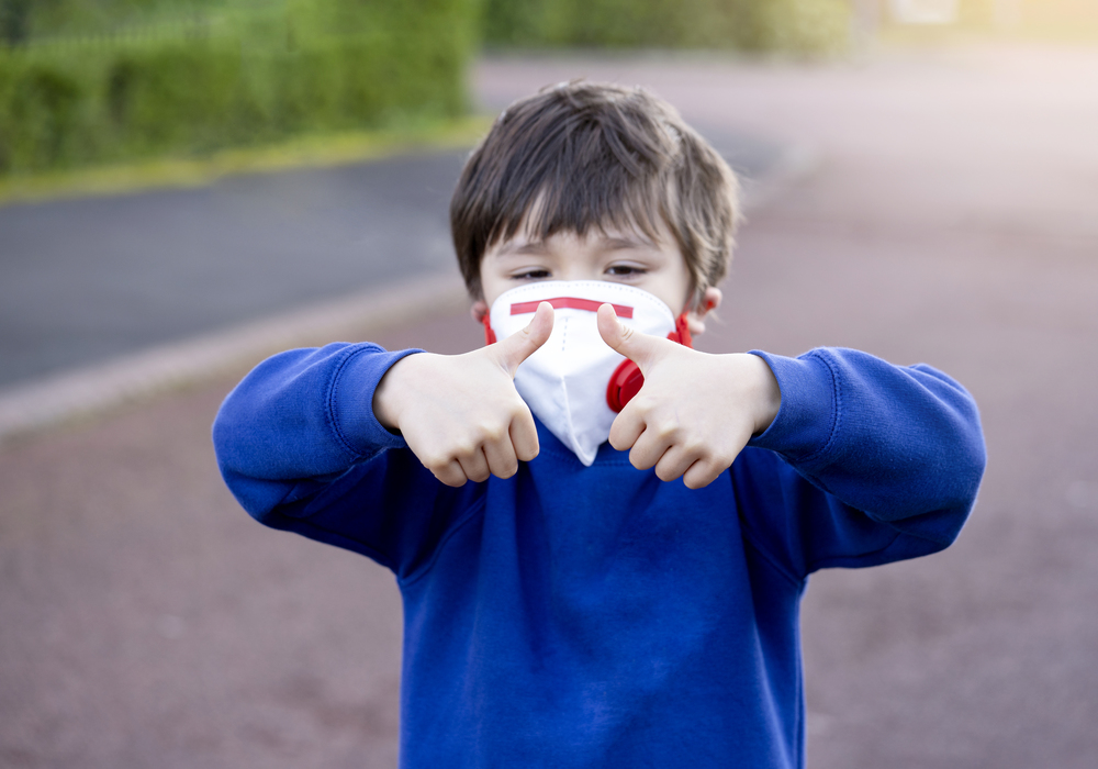 Selective focus School kid wearing protective face mask for pollution or virus, Blurry face of Child in school uniform wearing protection mask and showing thumbs up while walking to school.