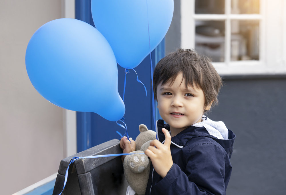 Cute little boy with teddy bear holding blue balloon with smiling face, Happy child playing with air balloons outdoor, Kid having fun playing outside in spring or summer