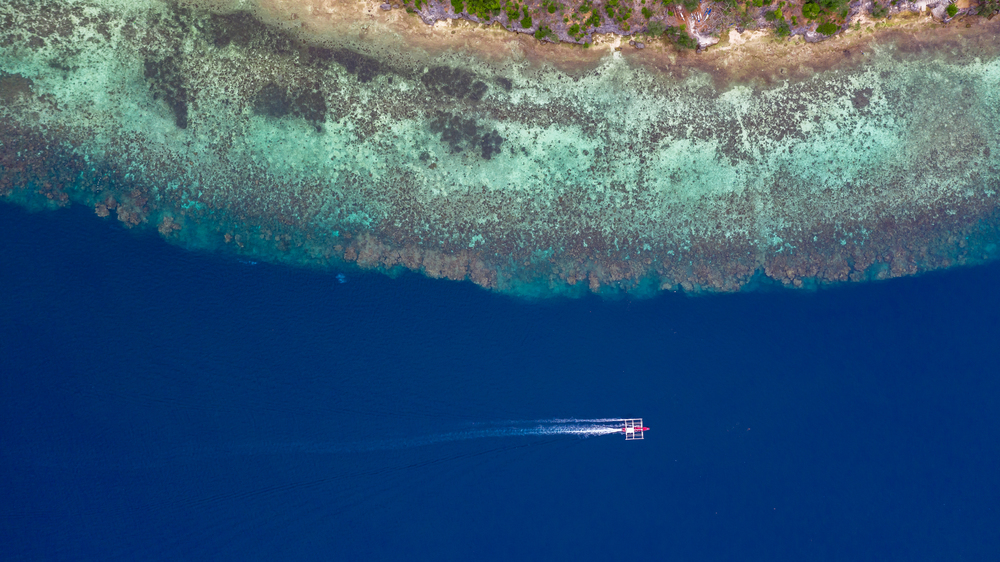 Aerial top down view of boat moving in open sea with clear and turquoise water on over coral reef,  Boat left the tropical lagoon, Moalboal, Oslob, Cebu Island, Philippines.