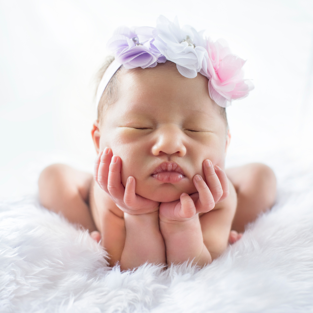 Newborn 7 day old baby girl on his white bed relaxing and flower on her head