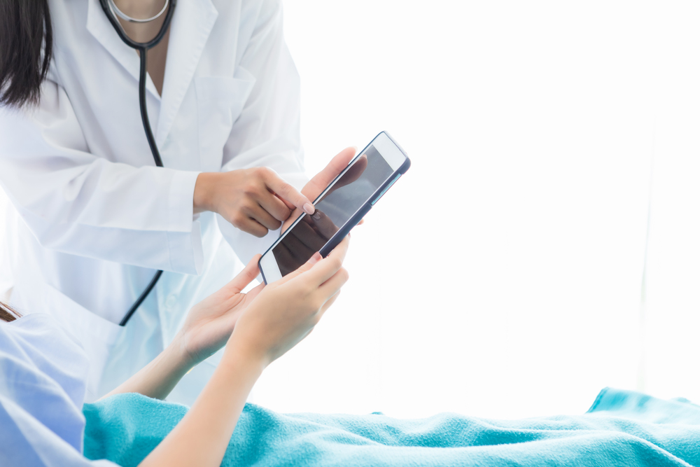 Close-up of Asian young female doctor therapeutic advising with tablet to Asian young female patient on Bed in hospital background.