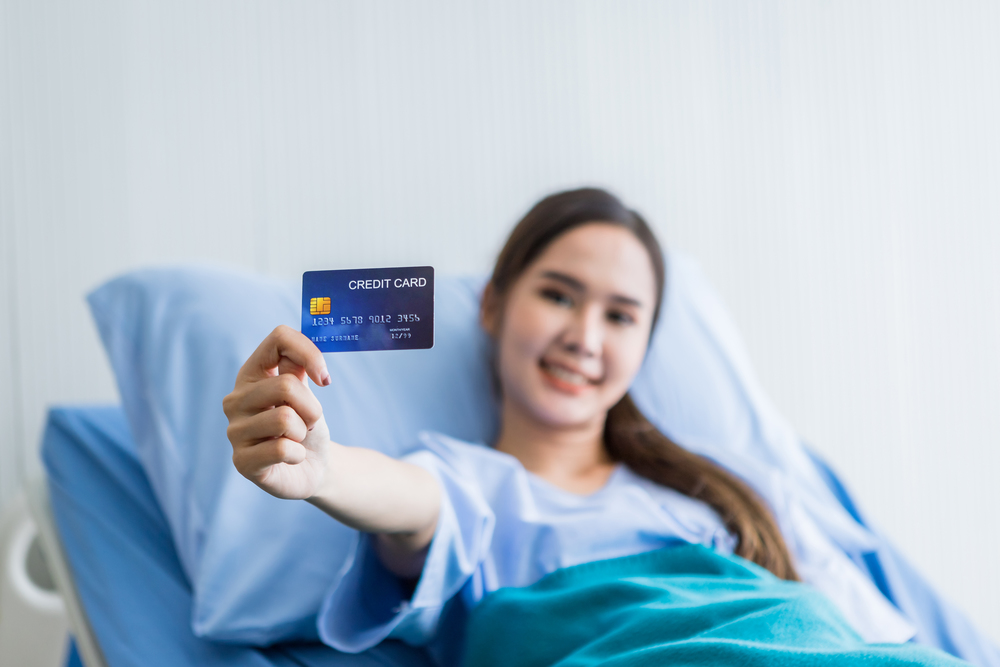 Asian young female patient smiley face Abstract blur with focus on show holding a credit card lying on bed in the room hospital background,payment medical treatment concept