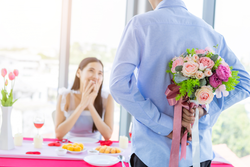Valentine&rsquo;s day and asian Young happy couple concept,Close up of asian a man holding a bouquet of roses woman with hands over her face awaits surprise after lunch In a restaurant background