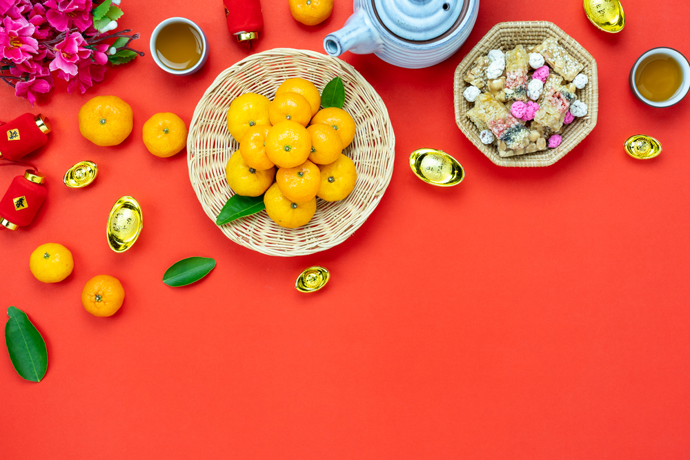 Chinese language mean rich or wealthy and happy.Table top view Lunar New Year & Chinese New Year concept background.Flat lay orange in wood basket & sweet dessert with blossom on  rustic red backdrop.