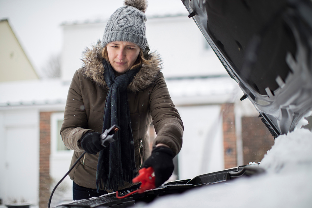 Woman Using Jumper Cables On Car Battery On Snowy Day