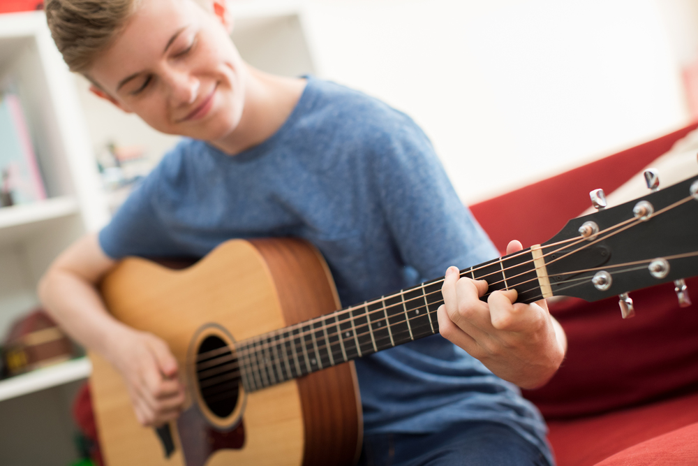 Teenage Boy Sitting On Sofa At Home Playing Guitar