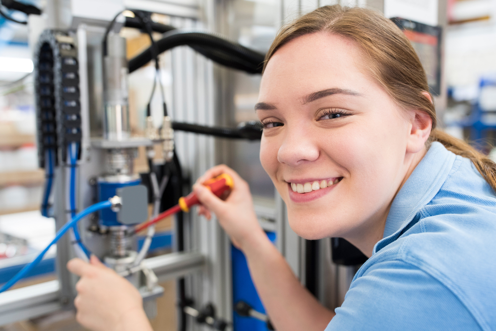 Portrait Of Female Apprentice Engineer Working On Machine In Factory