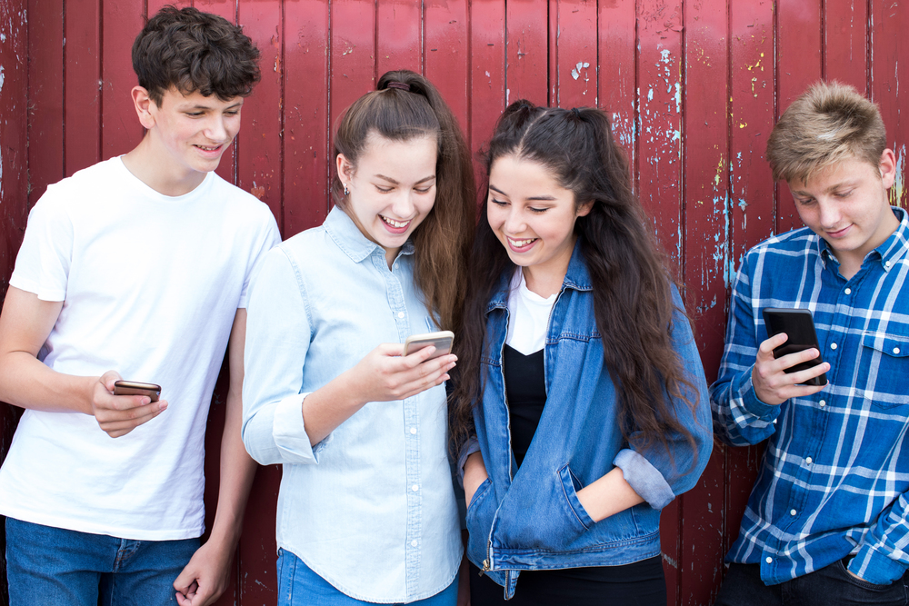 Group Of Teenage Froends Looking At Mobile Phones In Urban Setting
