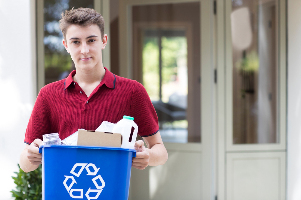 Portrait Of Teenage Boy Outside House Carrying Recycling Bin