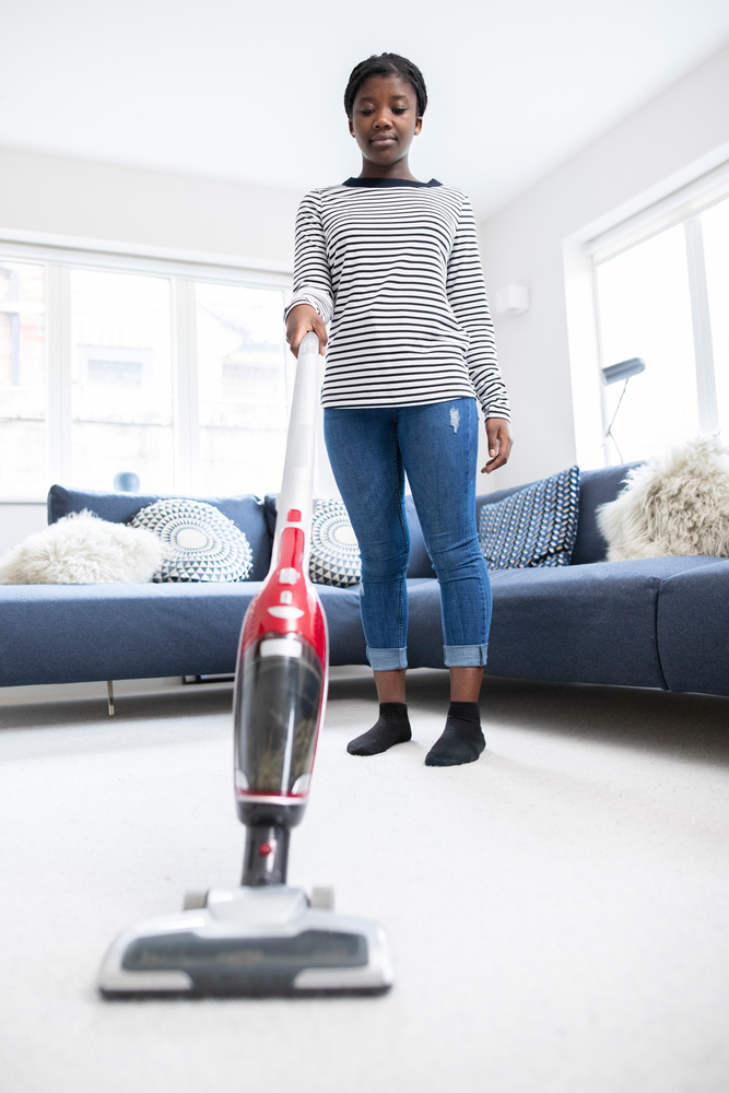 Teenage Girl Helping Out With Chores At Home Vacuuming Carpet In Lounge With Cordless Cleaner